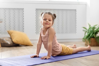 Photo of Little cute girl practicing yoga on mat at home