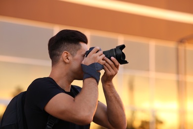 Photo of Photographer taking picture with professional camera on city street at sunset