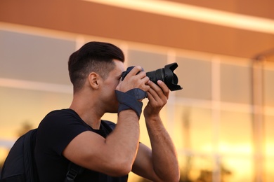 Photographer taking picture with professional camera on city street at sunset