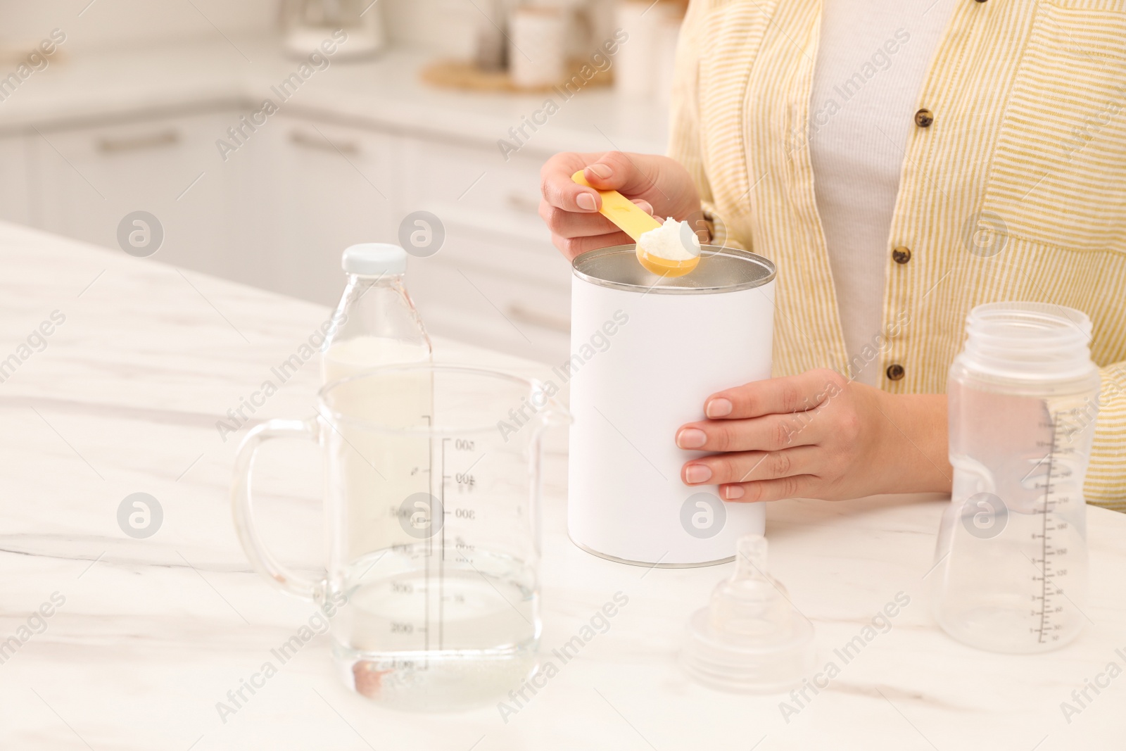 Photo of Woman preparing infant formula at table indoors, closeup. Baby milk