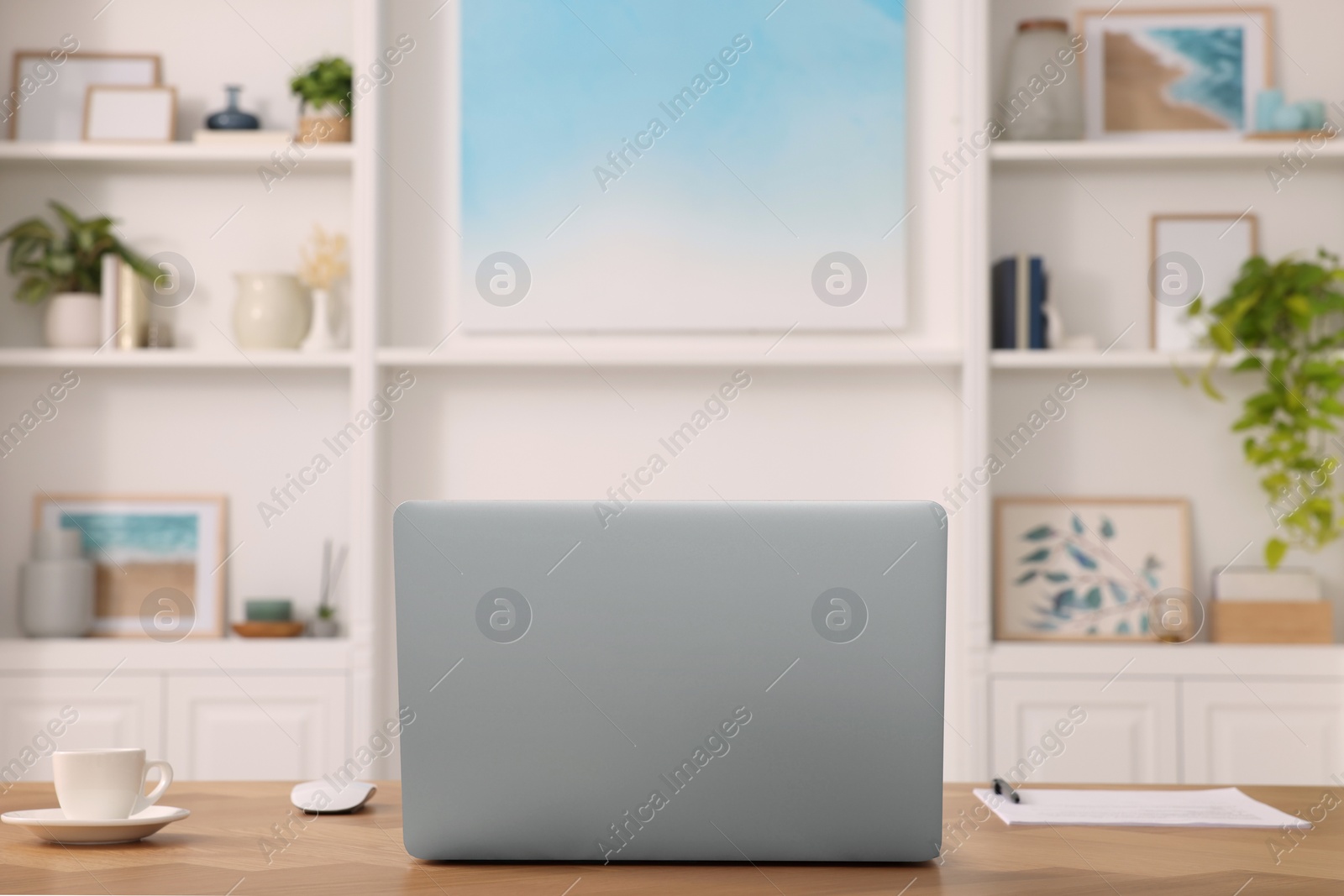 Photo of Interior design. Cosy workplace with laptop on wooden table near abstract picture between shelves