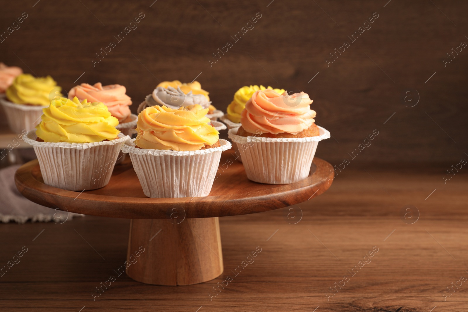 Photo of Stand with tasty cupcakes on wooden table. Space for text