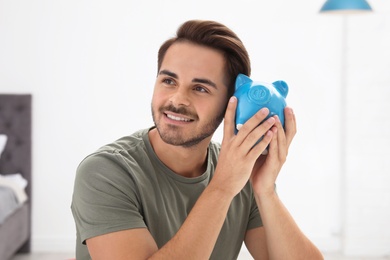 Happy young man with piggy bank indoors