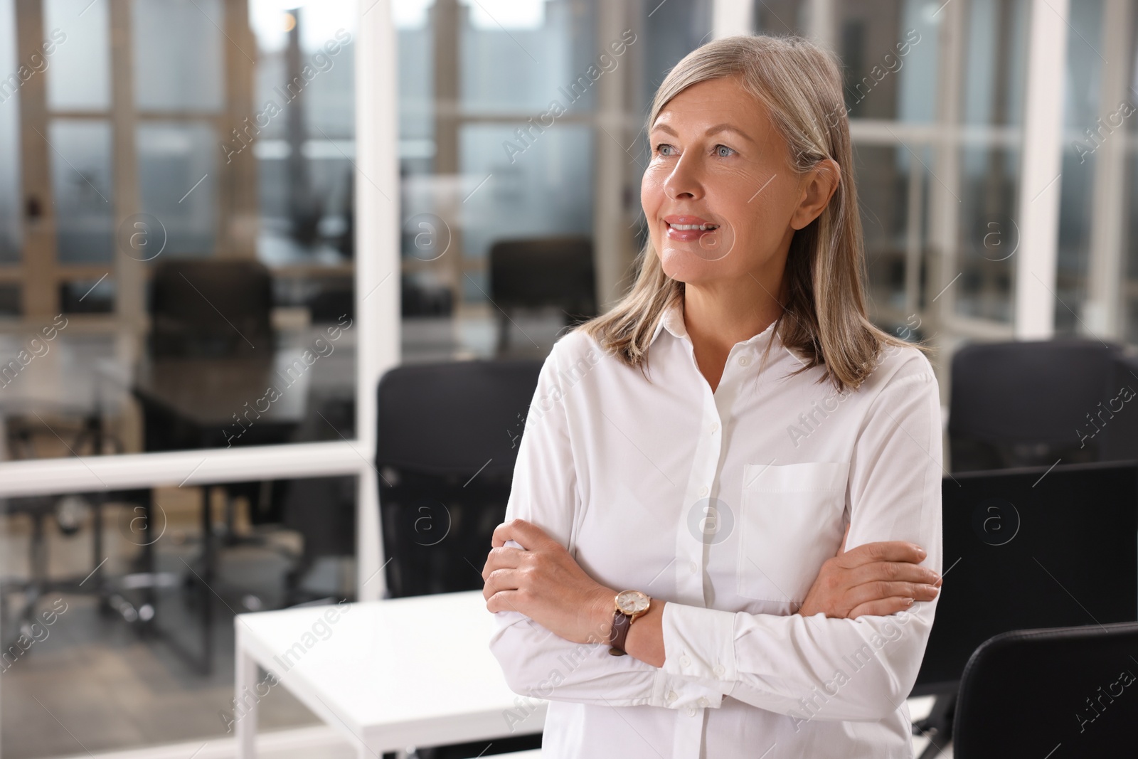 Photo of Smiling woman with crossed arms in office, space for text. Lawyer, businesswoman, accountant or manager