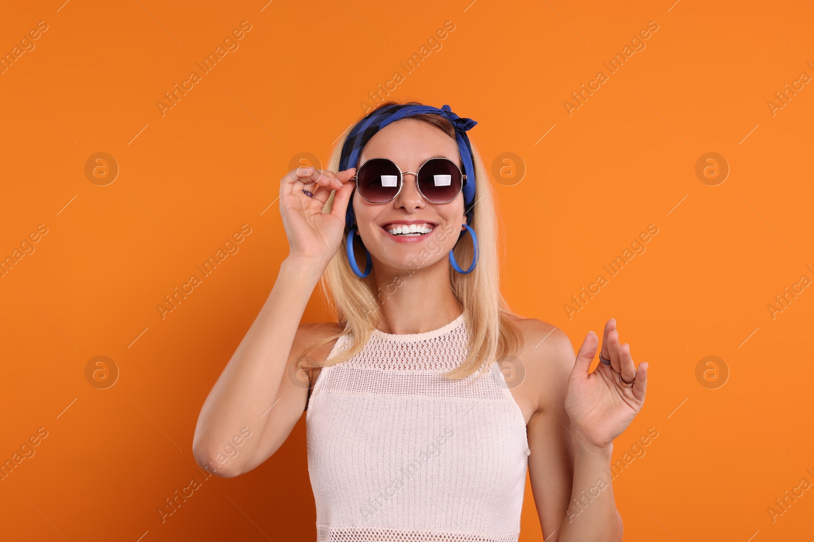 Photo of Portrait of smiling hippie woman in sunglasses on orange background