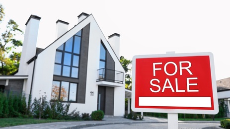 Photo of Red real estate sign near house outdoors on sunny day