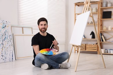 Photo of Man with brush and palette painting in studio. Using easel to hold canvas