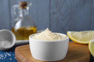 Photo of Tasty mayonnaise in bowl and lemon wedges on table, closeup