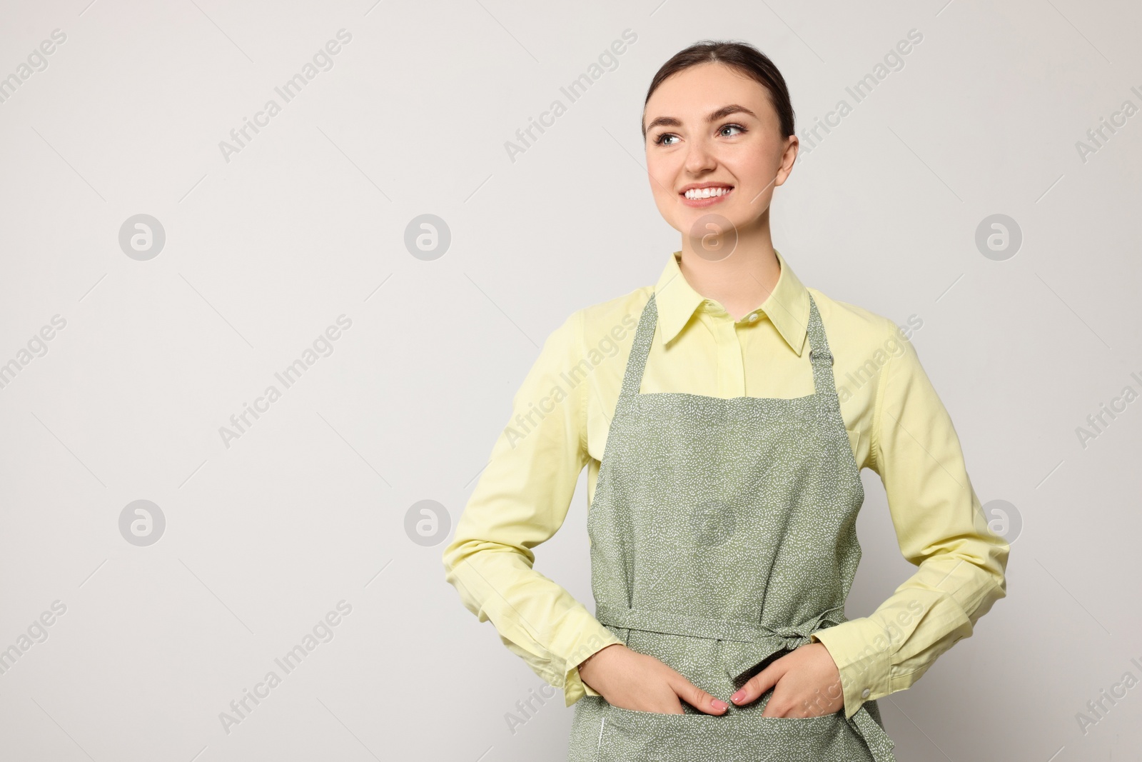 Photo of Beautiful young woman in clean apron with pattern on light grey background. Space for text