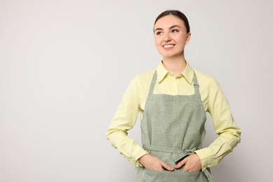 Photo of Beautiful young woman in clean apron with pattern on light grey background. Space for text