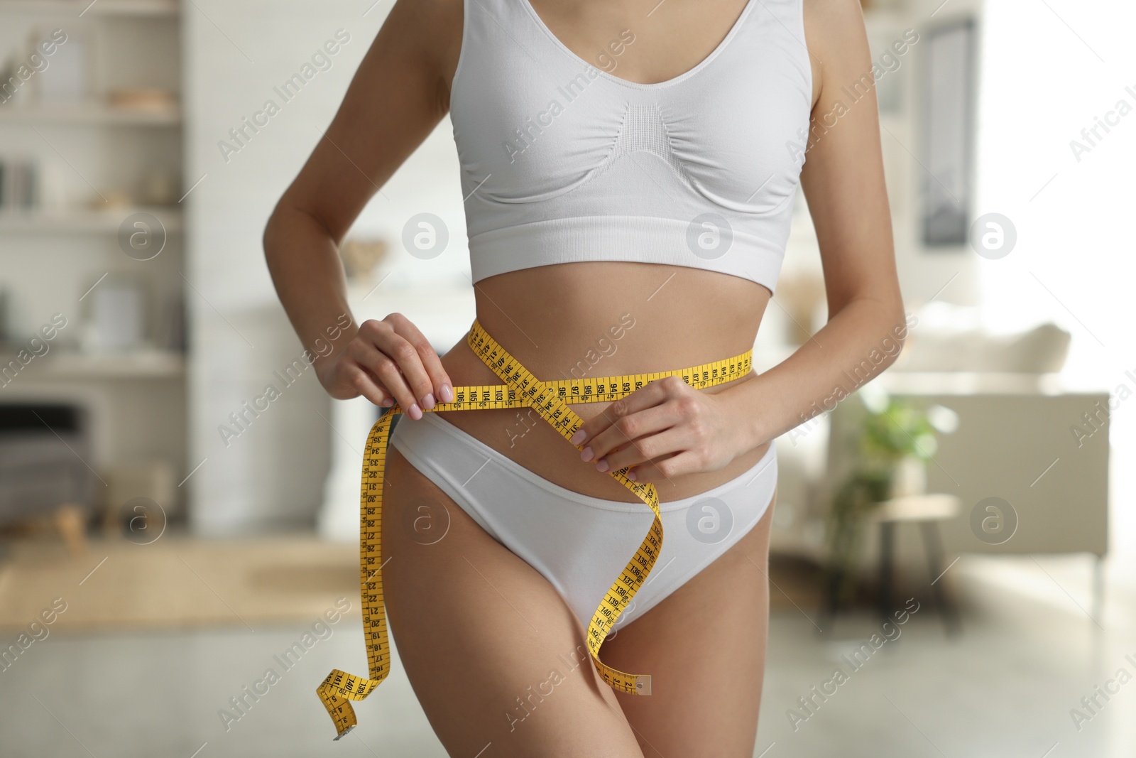 Photo of Young woman measuring waist with tape at home, closeup