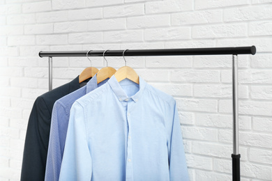 Photo of Rack with stylish men's clothes near white brick wall