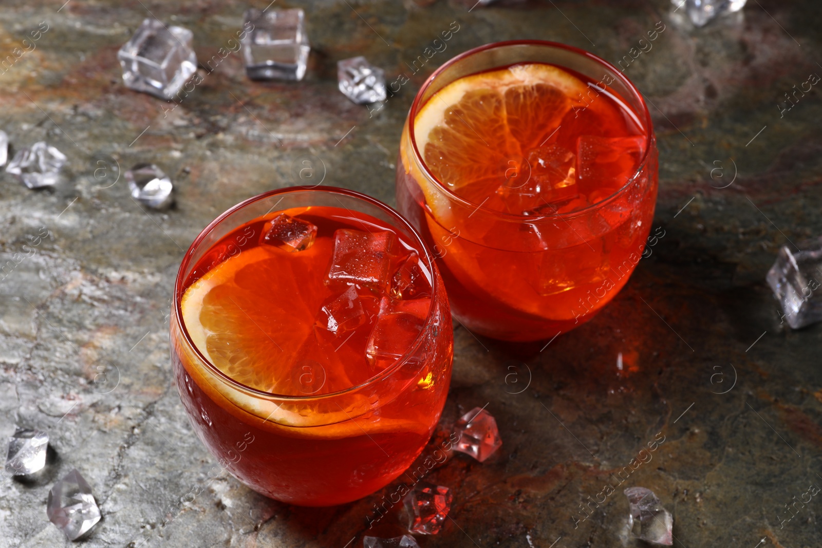 Photo of Aperol spritz cocktail, ice cubes and orange slices in glasses on grey textured table