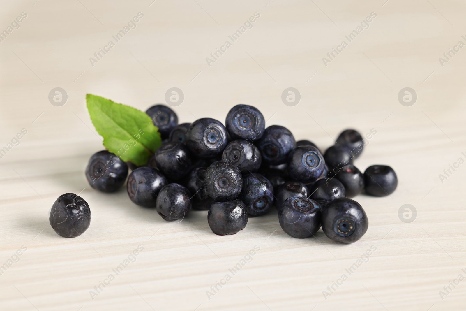 Photo of Pile of ripe bilberries and leaf on white wooden table, closeup