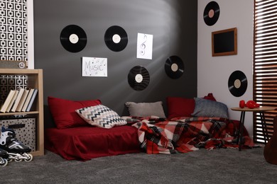 Photo of Stylish teenager's room with bed, wooden table and vinyl records on wall. Interior design