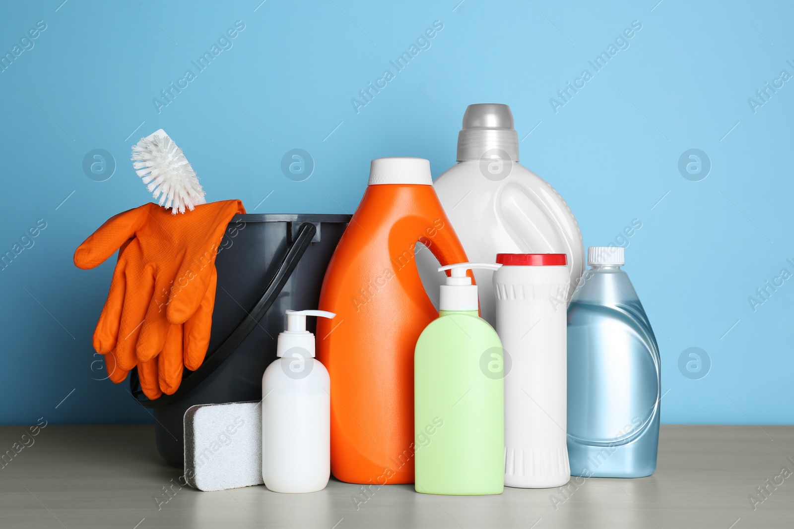 Photo of Different cleaning supplies and tools on wooden table against light blue background