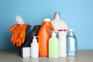 Photo of Different cleaning supplies and tools on wooden table against light blue background