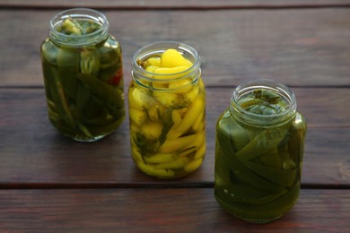 Photo of Glass jars of pickled green and yellow jalapeno peppers on wooden table