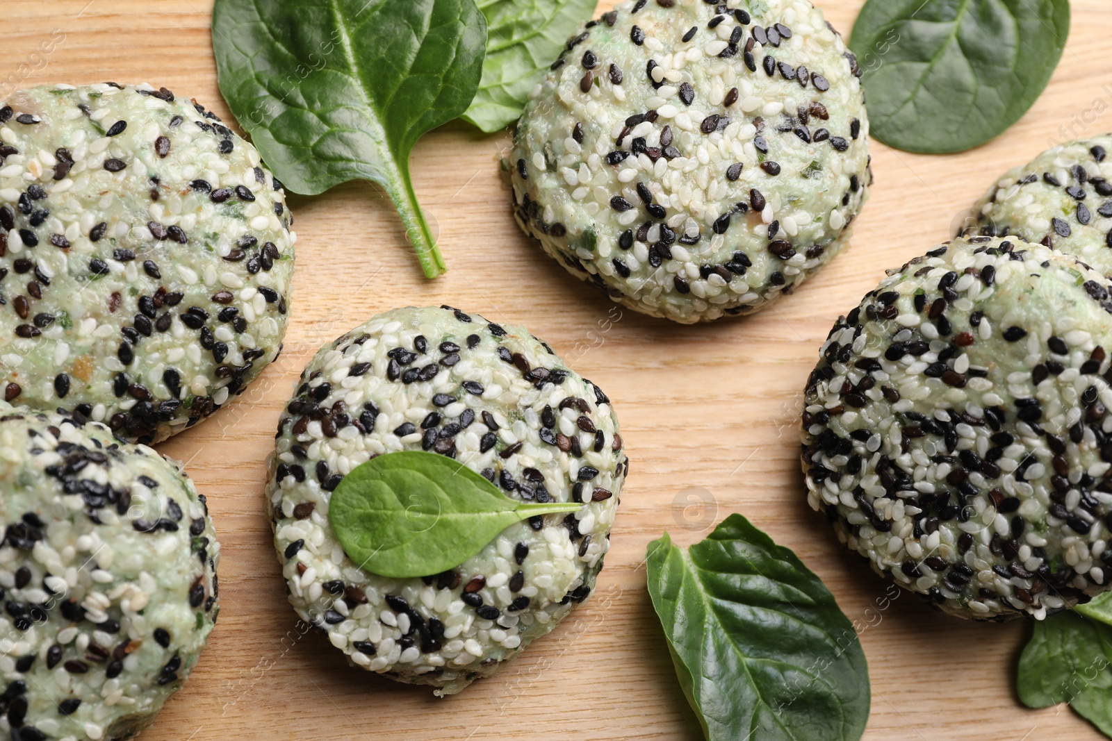 Photo of Tasty vegan cutlets with sesame seeds and spinach on wooden table, top view