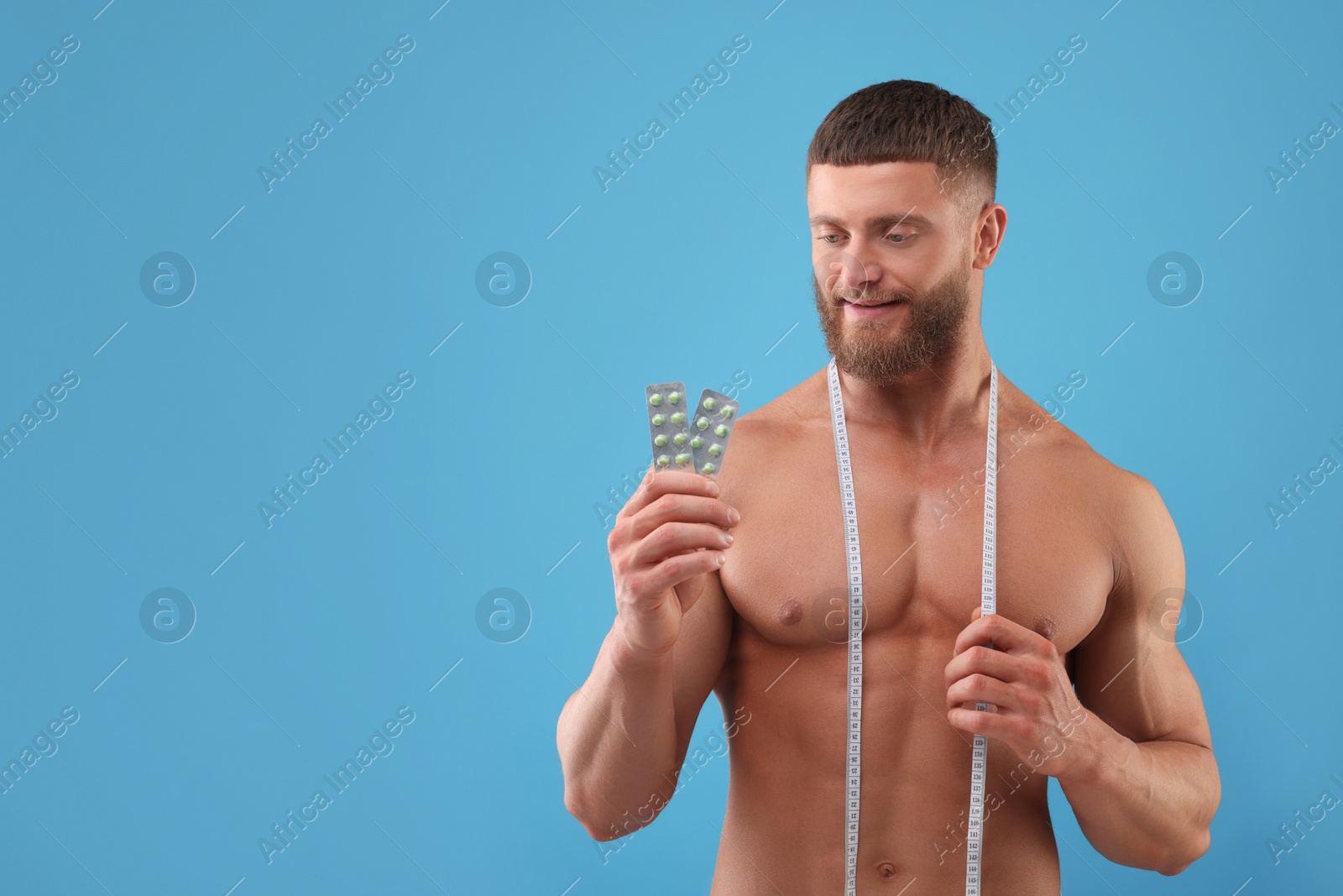 Photo of Athletic young man with measuring tape and pills on light blue background, space for text. Weight loss