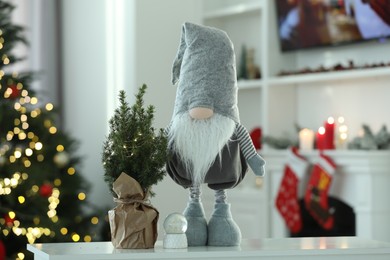 Photo of Funny Christmas gnome with small decorative tree on table indoors