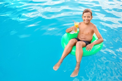 Photo of Happy cute boy on inflatable ring with drink in swimming pool