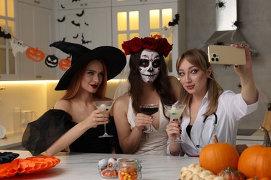 Photo of Group of women in scary costumes with cocktails taking selfie at Halloween party indoors