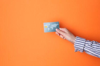 Woman holding credit card on orange background, closeup. Space for text