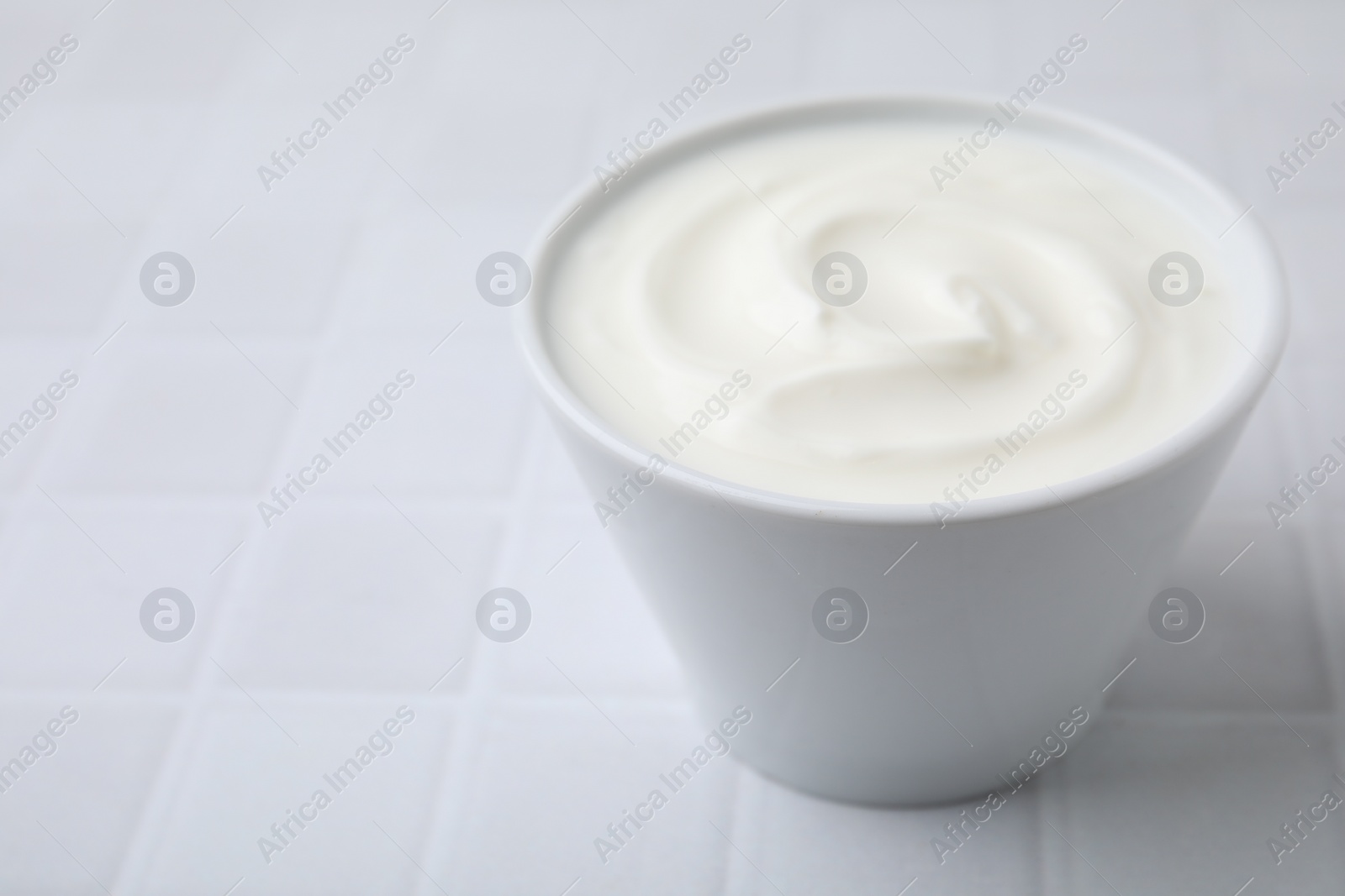 Photo of Delicious natural yogurt in bowl on white tiled table, closeup. Space for text