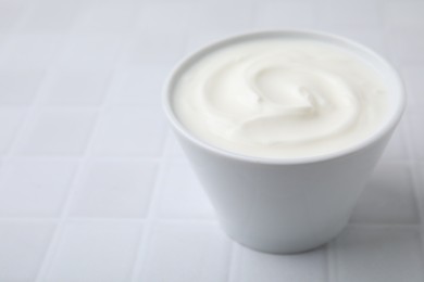 Delicious natural yogurt in bowl on white tiled table, closeup. Space for text