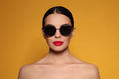 Attractive woman in fashionable sunglasses against orange background