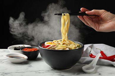 Photo of Woman eating delicious ramen with chopsticks at white marble table, closeup. Noodle soup