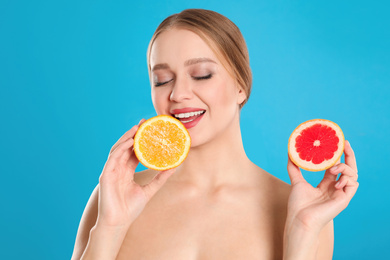 Photo of Young woman with cut grapefruit and orange on blue background. Vitamin rich food