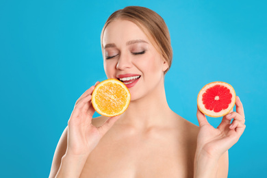 Young woman with cut grapefruit and orange on blue background. Vitamin rich food