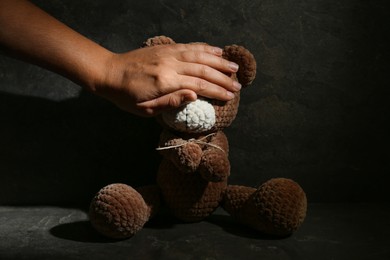 Photo of Stop child abuse. Woman covering bear's eyes in dark room, closeup