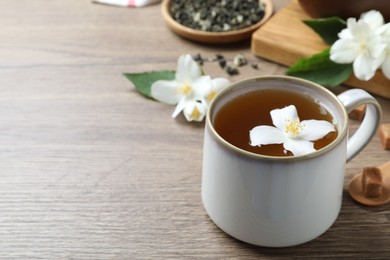 Photo of Cup of tea with fresh jasmine flower on wooden table. Space for text