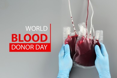 Image of World Donor Day. Doctor in gloves holding blood packs on grey background, top view 