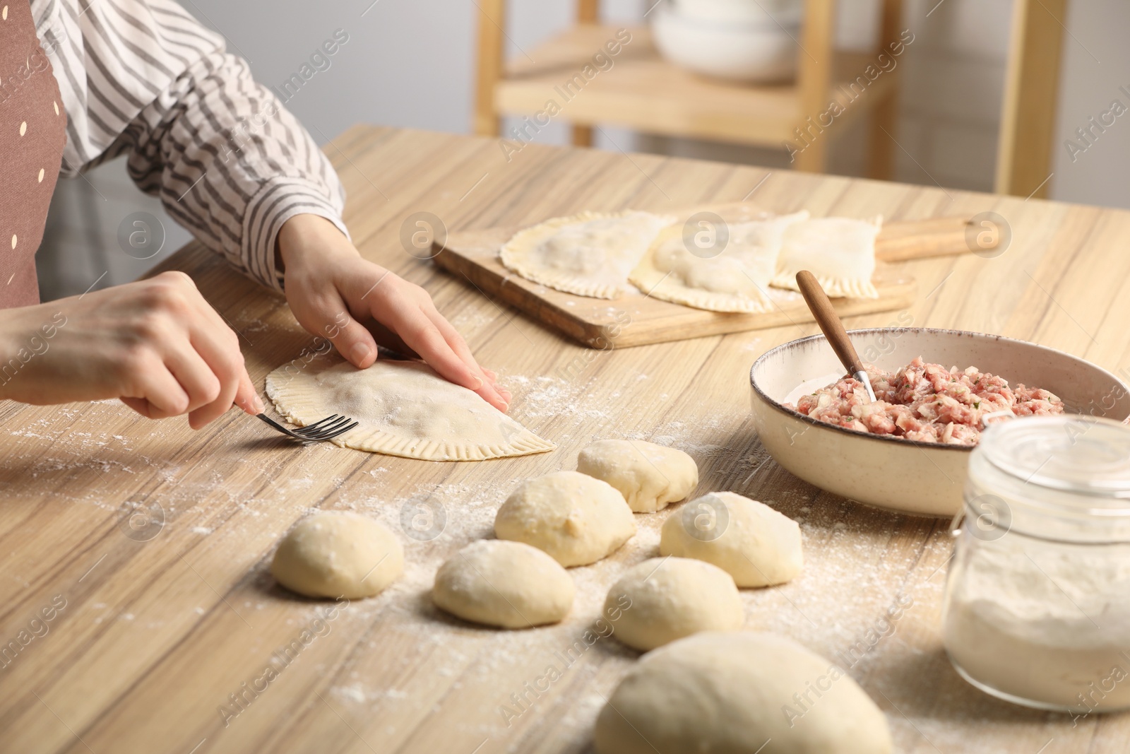 Photo of Woman making chebureki at wooden table indoors, closeup