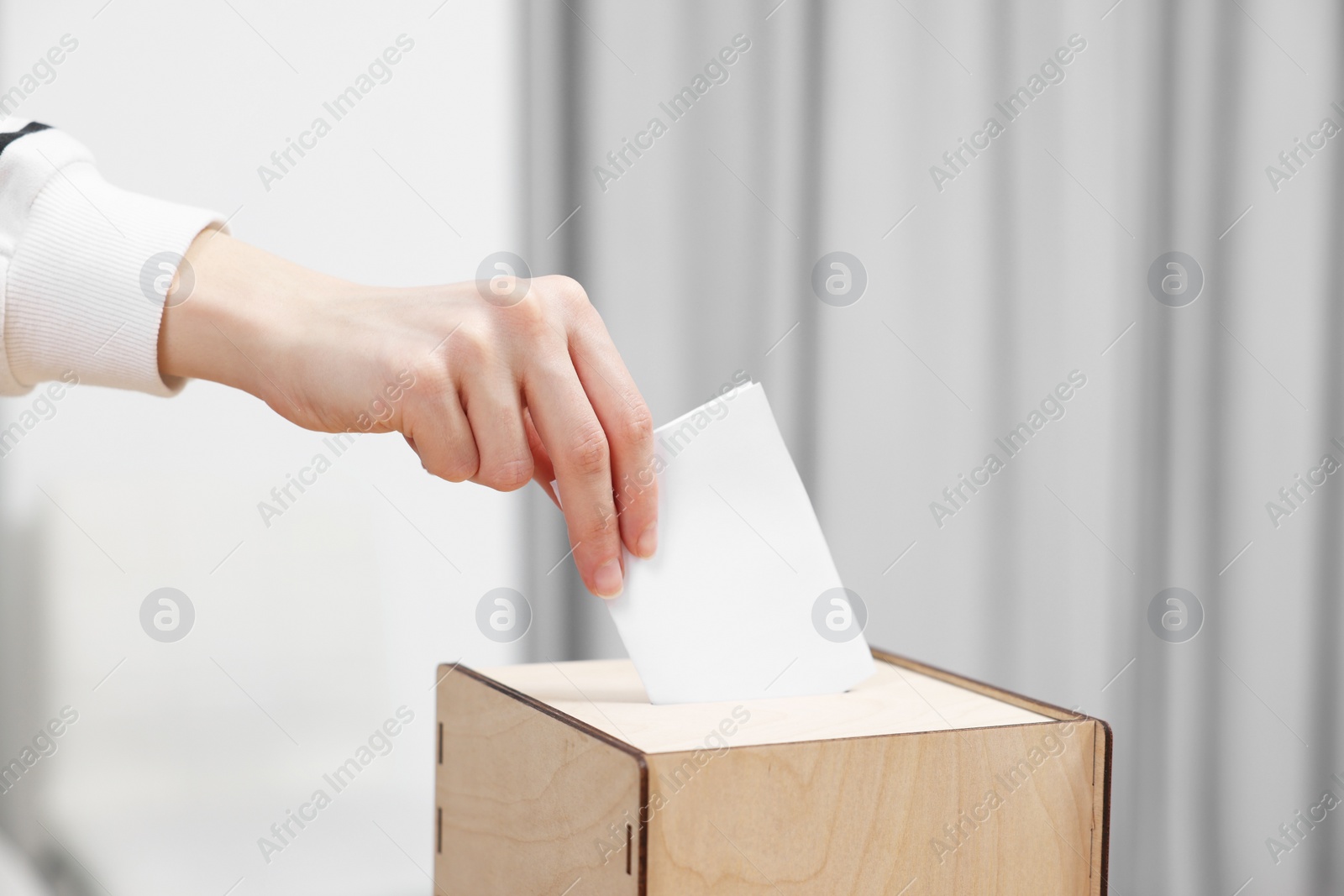 Photo of Woman putting her vote into ballot box on blurred background, closeup