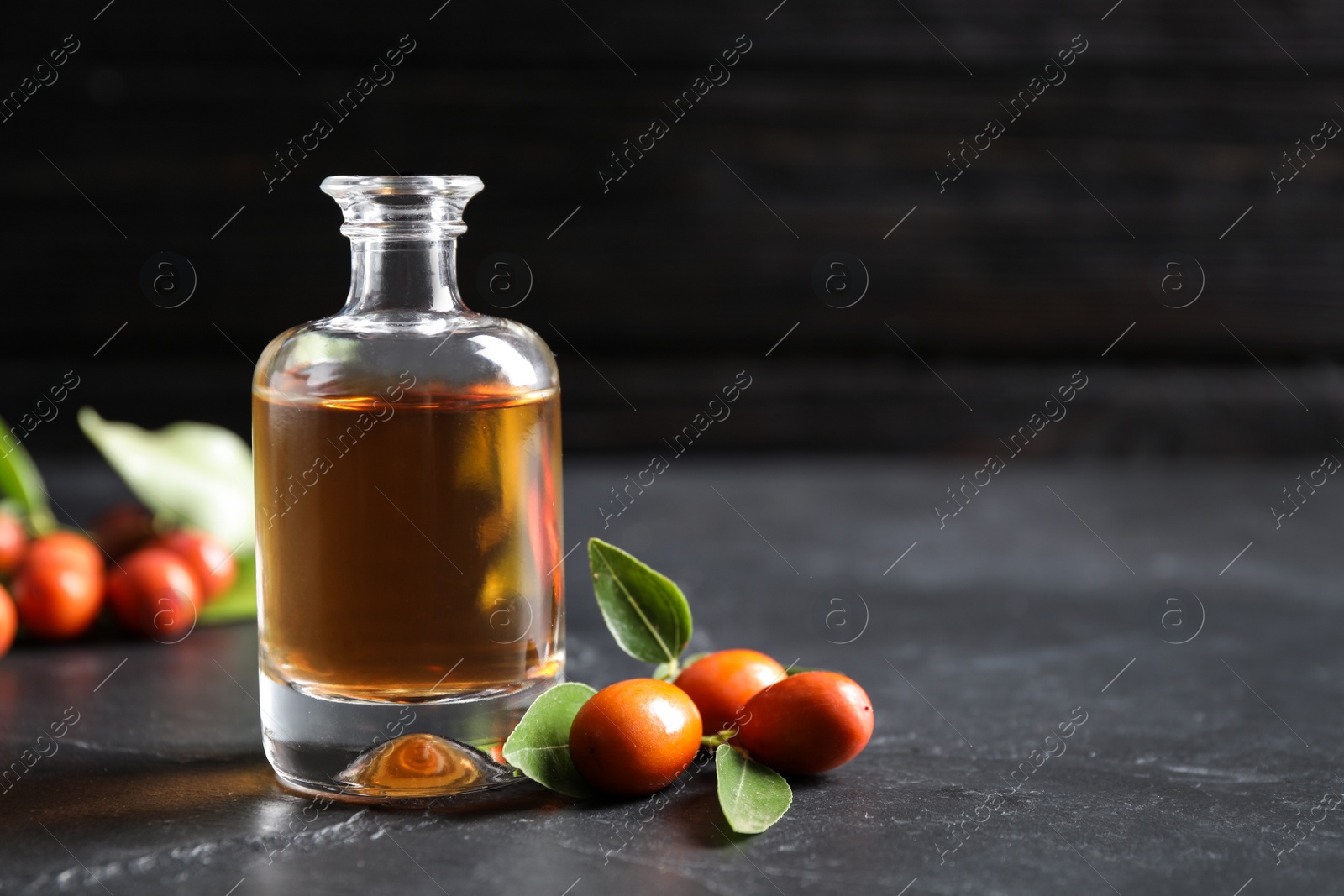 Photo of Glass bottle with jojoba oil and seeds on grey stone table against dark background. Space for text