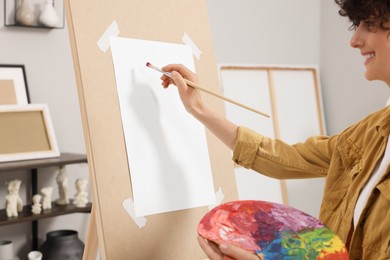 Photo of Young woman painting on easel with paper in studio, closeup