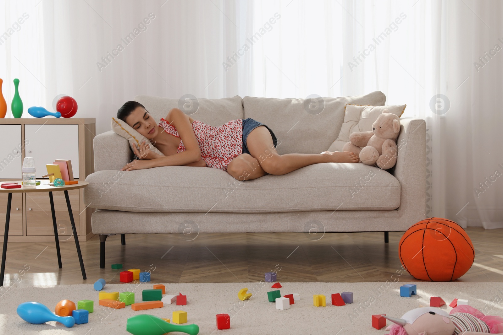 Photo of Tired young mother sleeping on sofa in messy living room