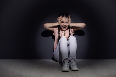 Photo of Depressed little girl sitting on floor indoors. Time to visit child psychologist