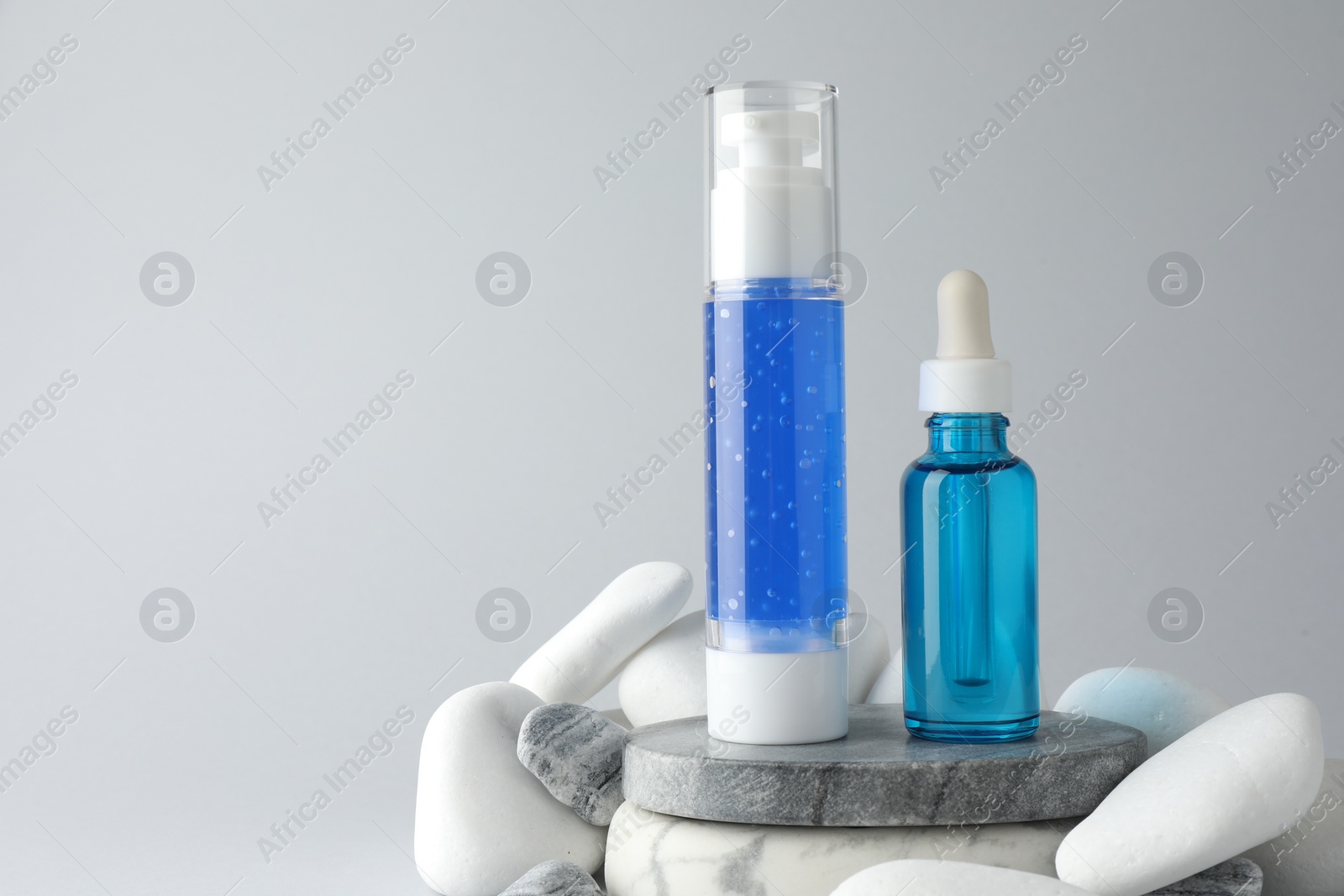 Photo of Bottles of cosmetic products and stones on light grey background. Space for text