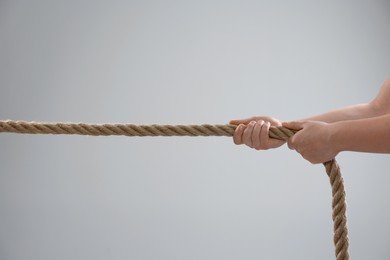 Photo of Dispute concept. Man pulling rope on light grey background, closeup
