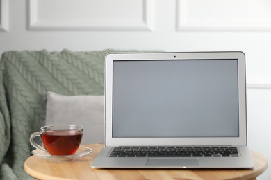 Photo of Modern laptop and cup of tea on wooden table indoors