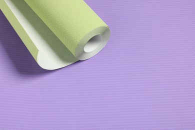 Photo of One green wallpaper roll on violet sample, space for text