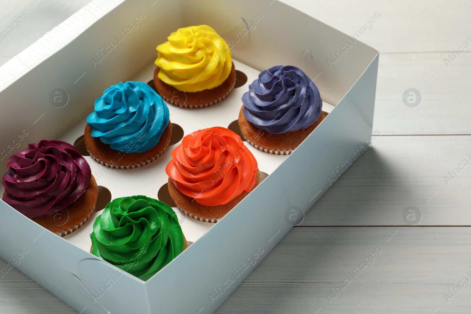 Photo of Box with different cupcakes on white wooden table, closeup