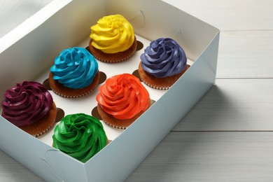 Photo of Box with different cupcakes on white wooden table, closeup