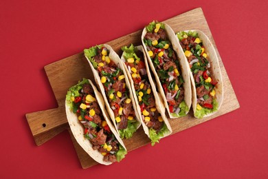 Delicious tacos with meat and vegetables on red table, top view